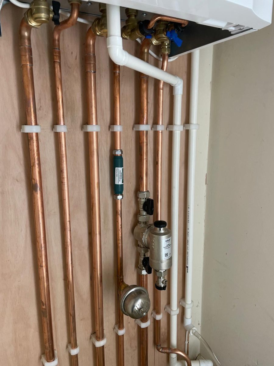 Close-up of copper pipework, isolation valves and a magnetic filter beneath a boiler