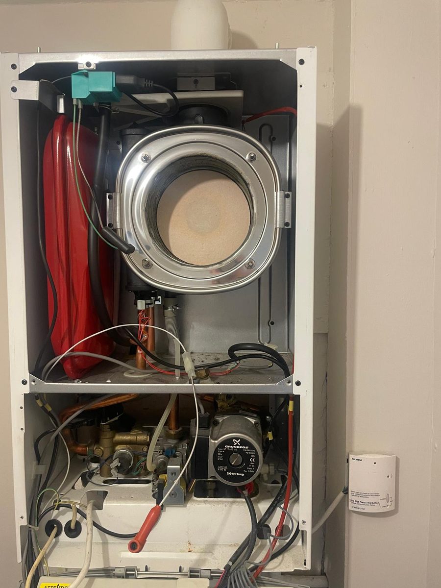 Combi boiler with the cover removed during a service, showing the fan, expansion vessel and pump