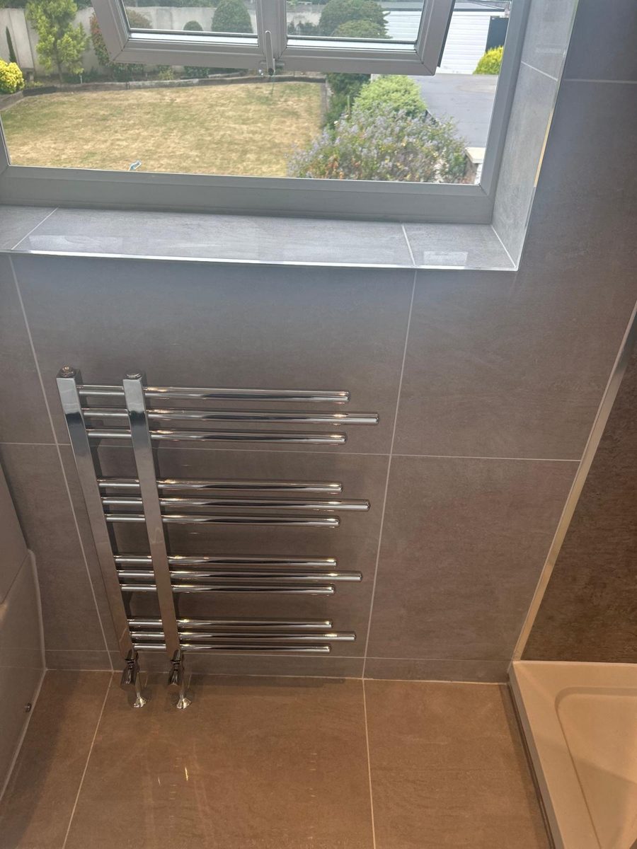 Chrome heated towel radiator fitted in a tiled bathroom