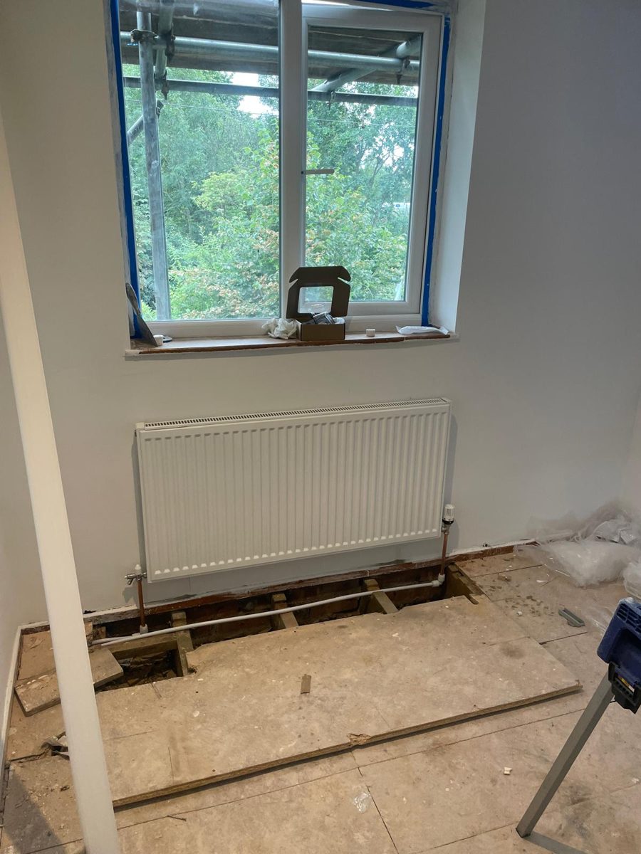 Radiator installation in progress with floorboards lifted for new pipe runs